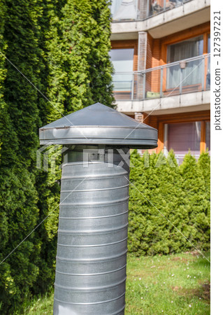 Metal Ventilation Pipe with Cap in Residential Courtyard Near Evergreen Trees 127397221