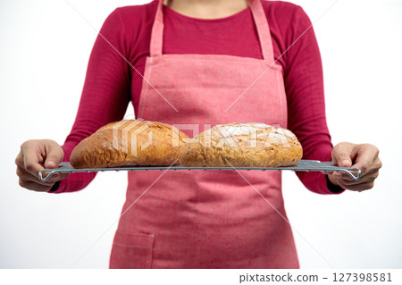 Woman in red apron holding wire rack with two freshly baked crusty loaves of bread, showing golden brown color and homemade rustic texture Woman in red apron holding wire rack with two freshly baked crusty loaves of bread, showing golden brown color and homemade rustic texture 127398581