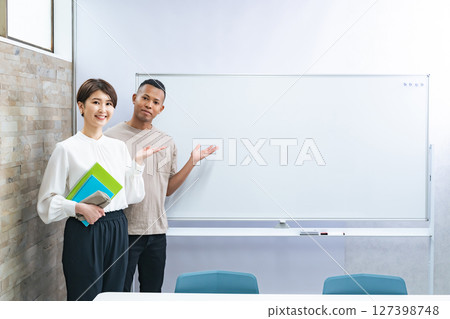 A black man and a Japanese woman standing in front of a whiteboard in a classroom 127398748