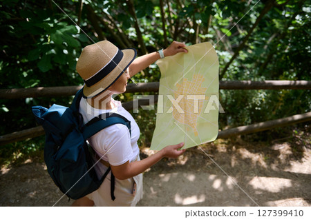 Woman Explorer Holding Map in Forested Pathway During Daytime Journey Woman Explorer Holding Map in Forested Pathway During Daytime Journey 127399410