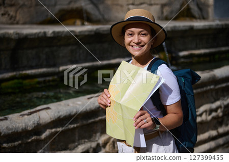 Woman Smiling While Holding a Map During Travel Exploration in a Scenic Outdoor Location 127399455