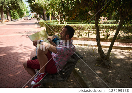 Man Relaxing on Park Bench Holding Map During Sunny Day 127399588