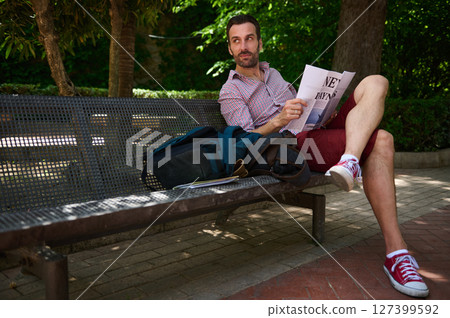 Man Enjoying Leisurely Reading on a Park Bench in a Serene Outdoor Setting Man Enjoying Leisurely Reading on a Park Bench in a Serene Outdoor Setting 127399592