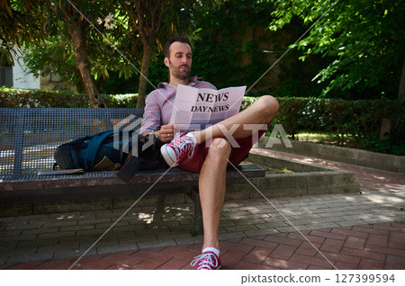 Man Reading a Newspaper Outdoors on a Park Bench in a Sunny Garden Man Reading a Newspaper Outdoors on a Park Bench in a Sunny Garden 127399594