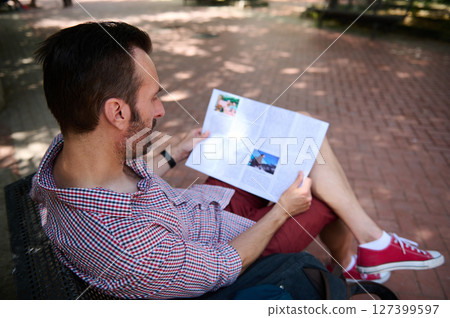 Man Relaxing on Bench while Reading a Magazine in Outdoor Park Setting 127399597