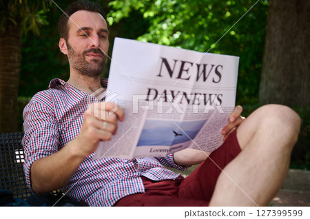 Man Relaxing Outdoors Reading a Newspaper on a Sunny Day in a Park 127399599