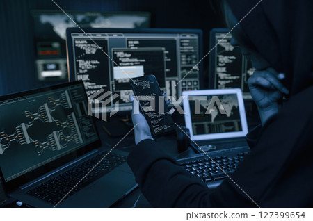 Holding smartphone with code. Young professional female hacker is indoors by computer with lot of information on displays 127399654