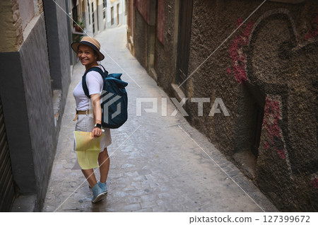 Young Woman Tourist Exploring a Historic European Alleyway with a Map and Backpack Young Woman Tourist Exploring a Historic European Alleyway with a Map and Backpack 127399672