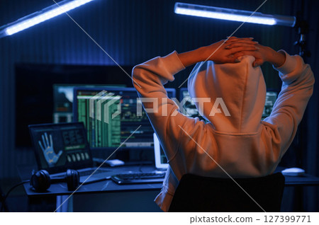 Looking at screens. Young professional female hacker is indoors by computer with lot of information on displays 127399771