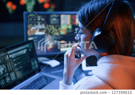 Focused on work. Young professional female hacker is indoors by computer with lot of information on displays Focused on work. Young professional female hacker is indoors by computer with lot of information on displays 127399810