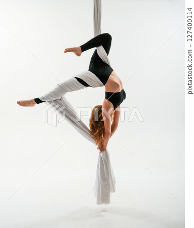 Hanging upside down. Young beautiful woman doing fly yoga against white background Hanging upside down. Young beautiful woman doing fly yoga against white background 127400114