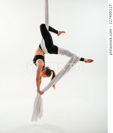 Hanging upside down. Young beautiful woman doing fly yoga against white background Hanging upside down. Young beautiful woman doing fly yoga against white background 127400117