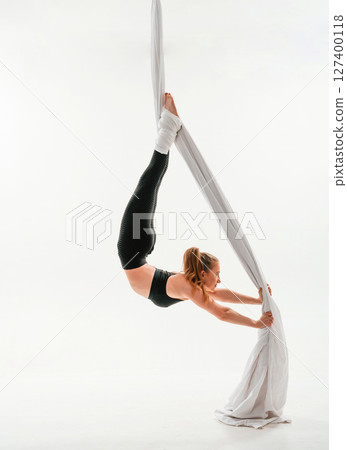 In black sportswear, stretching. Young beautiful woman doing fly yoga against white background In black sportswear, stretching. Young beautiful woman doing fly yoga against white background 127400118
