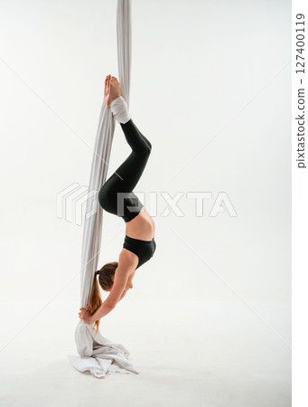 Hanging upside down. Young beautiful woman doing fly yoga against white background 127400119
