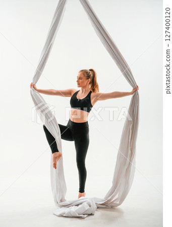 In black sportswear, stretching. Young beautiful woman doing fly yoga against white background 127400120
