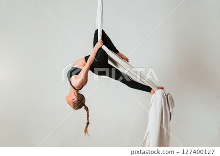 In the midair. Young beautiful woman doing fly yoga against white background In the midair. Young beautiful woman doing fly yoga against white background 127400127