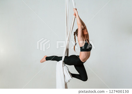 In the midair. Young beautiful woman doing fly yoga against white background In the midair. Young beautiful woman doing fly yoga against white background 127400130