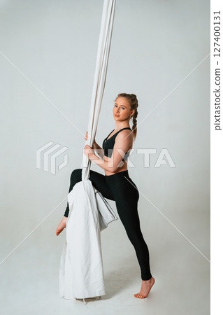 In black sportswear, stretching. Young beautiful woman doing fly yoga against white background 127400131