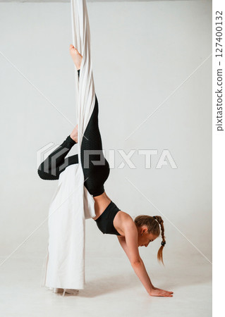 In black sportswear, stretching. Young beautiful woman doing fly yoga against white background In black sportswear, stretching. Young beautiful woman doing fly yoga against white background 127400132