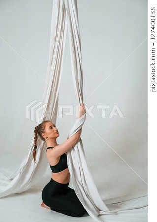 Sitting, taking a rest, holding canvas. Young beautiful woman doing fly yoga against white background Sitting, taking a rest, holding canvas. Young beautiful woman doing fly yoga against white background 127400138