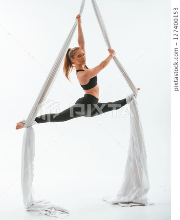 Stretching the legs. Young beautiful woman doing fly yoga against white background Stretching the legs. Young beautiful woman doing fly yoga against white background 127400153