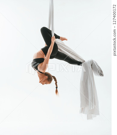 View from the side, hanging upside down. Young beautiful woman doing fly yoga against white background View from the side, hanging upside down. Young beautiful woman doing fly yoga against white background 127400172