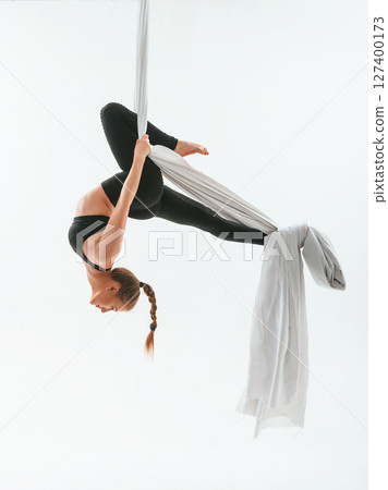 View from the side, hanging upside down. Young beautiful woman doing fly yoga against white background View from the side, hanging upside down. Young beautiful woman doing fly yoga against white background 127400173