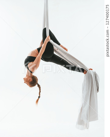 View from the side, hanging upside down. Young beautiful woman doing fly yoga against white background View from the side, hanging upside down. Young beautiful woman doing fly yoga against white background 127400175