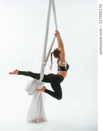 Strong arms and legs. In the midair. Young beautiful woman doing fly yoga against white background Strong arms and legs. In the midair. Young beautiful woman doing fly yoga against white background 127400176