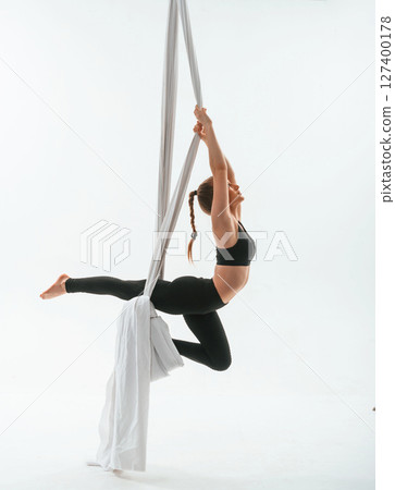 Strong arms and legs. In the midair. Young beautiful woman doing fly yoga against white background Strong arms and legs. In the midair. Young beautiful woman doing fly yoga against white background 127400178