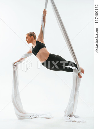 Professional occupation. Young beautiful woman doing fly yoga against white background Professional occupation. Young beautiful woman doing fly yoga against white background 127400182
