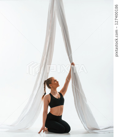 Sitting, taking a rest, holding canvas. Young beautiful woman doing fly yoga against white background Sitting, taking a rest, holding canvas. Young beautiful woman doing fly yoga against white background 127400186