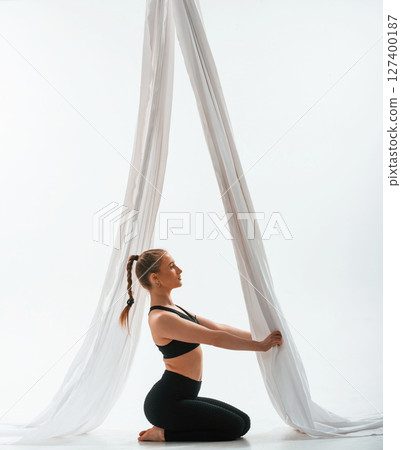 Sitting, holding canvas, side view. Young beautiful woman doing fly yoga against white background 127400187