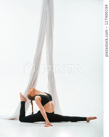 Sitting on the floor. Young beautiful woman doing fly yoga against white background Sitting on the floor. Young beautiful woman doing fly yoga against white background 127400194