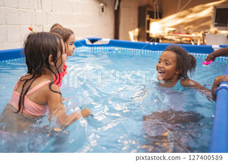 Children play joyfully in a backyard pool during summer afternoon Children play joyfully in a backyard pool during summer afternoon 127400589