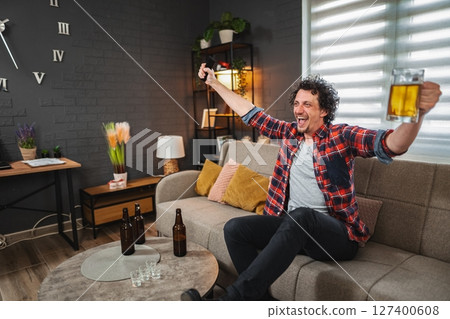 Excited man celebrating watching sports on tv with beer 127400608