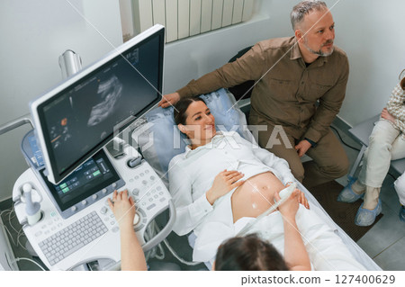 Man is sitting with his wife. Pregnant woman is lying down in the hospital, doctor does ultrasound 127400629