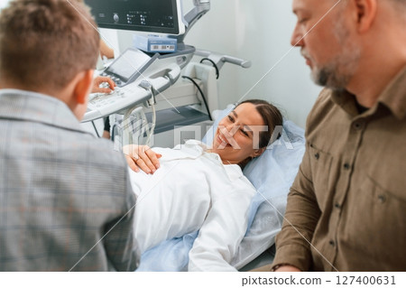 Son and husband are supporting mother. Pregnant woman is lying down in the hospital, doctor does ultrasound Son and husband are supporting mother. Pregnant woman is lying down in the hospital, doctor does ultrasound 127400631