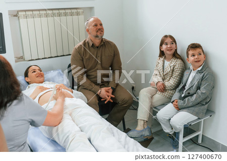 Family is sitting together. Pregnant woman is lying down in the hospital, doctor does ultrasound 127400670