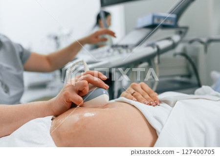 Focused close up view. Pregnant woman is lying down in the hospital, doctor does ultrasound Focused close up view. Pregnant woman is lying down in the hospital, doctor does ultrasound 127400705