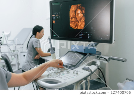 Nurse is working in the clinic, doing an ultrasound scan of the belly of a pregnant woman. Display with little baby Nurse is working in the clinic, doing an ultrasound scan of the belly of a pregnant woman. Display with little baby 127400706