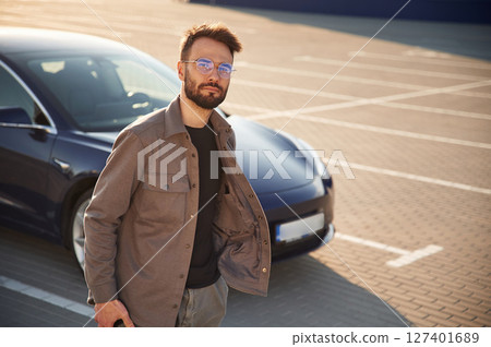 In glasses. Man is standing near his electric car outdoors 127401689