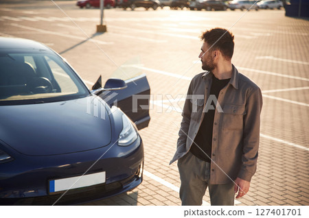 Front view. Man is standing near his electric car outdoors 127401701