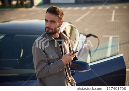 Charging the automobile. Man is standing near his electric car outdoors Charging the automobile. Man is standing near his electric car outdoors 127401708
