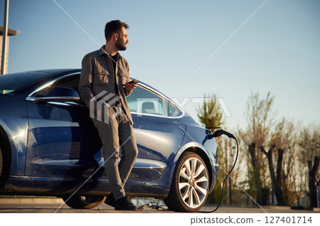 Standing and waiting for his automobile to charge. Man is near his electric car outdoors 127401714
