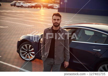 Sunny background. Man is standing near his electric car outdoors Sunny background. Man is standing near his electric car outdoors 127401735