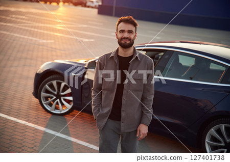 Sunny background. Man is standing near his electric car outdoors 127401738