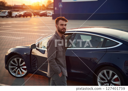 Gorgeous stylish man is standing near his electric car outdoors Gorgeous stylish man is standing near his electric car outdoors 127401739
