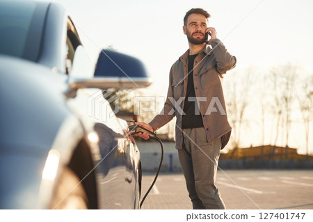 Business call by phone. Man is standing near his electric car outdoors 127401747