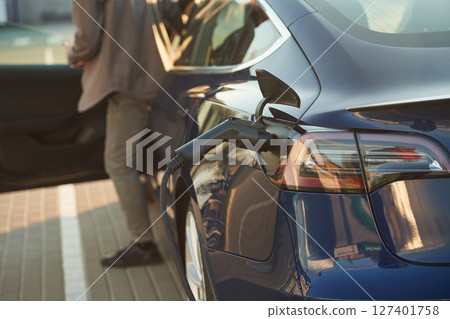 Rear part of the automobile that is charging. Man is standing near his electric car outdoors Rear part of the automobile that is charging. Man is standing near his electric car outdoors 127401758